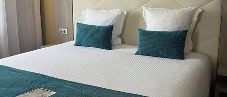 A hotel room with a large bed, two pillows, a bedside lamp, and a window with curtains.