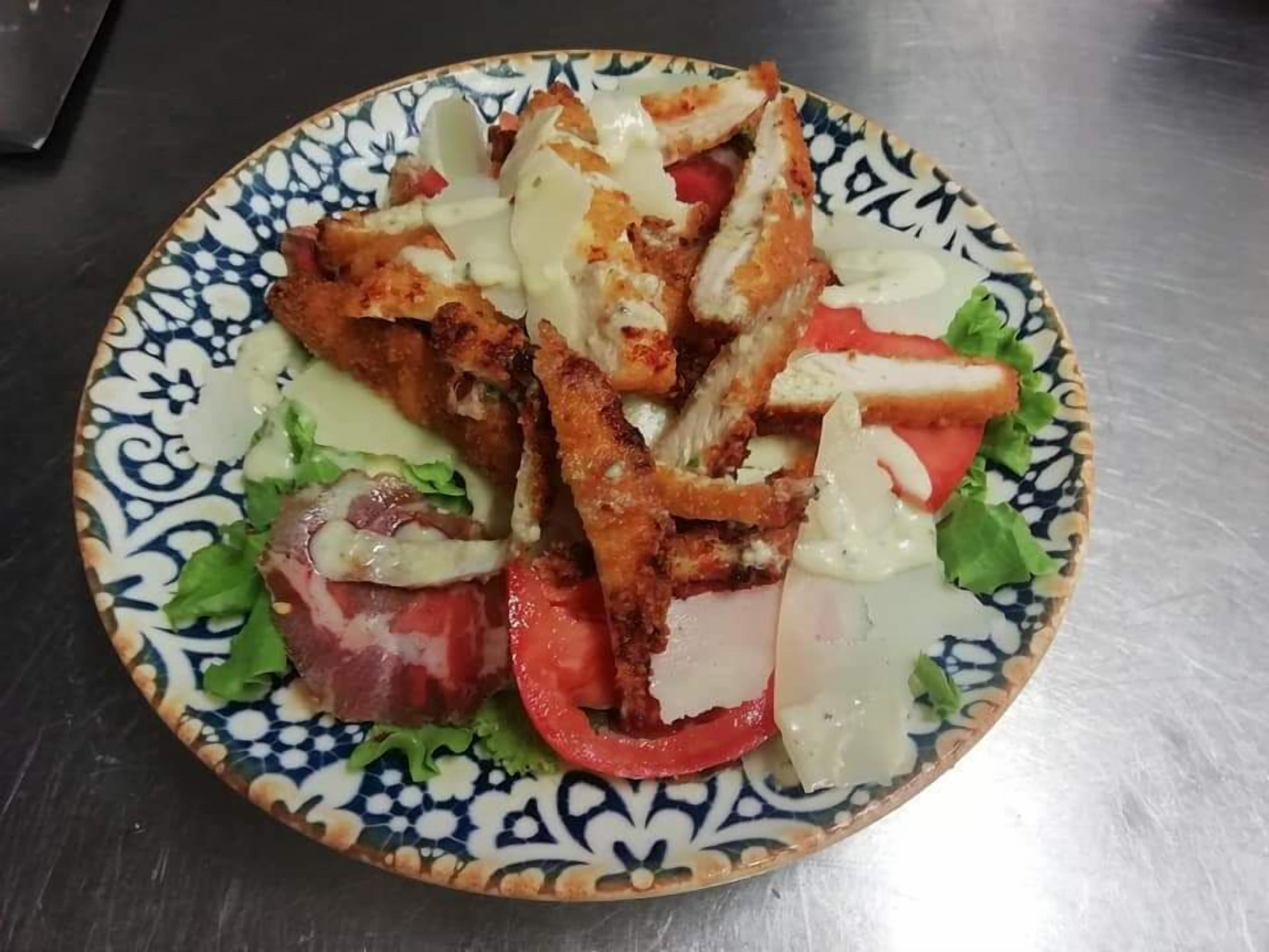 A plate of food with breaded chicken, tomatoes, lettuce, and a creamy sauce.