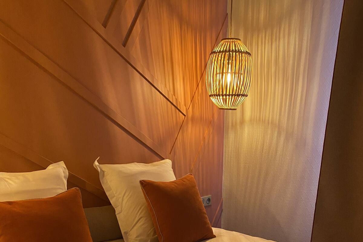 A neatly made bed with white and brown pillows, a brown throw blanket, and a hanging light fixture.