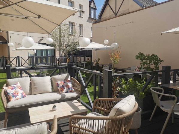 Un área de estar al aire libre con muebles de mimbre, un sofá con cojines estampados y sombrillas que dan sombra.