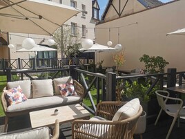 Un área de estar al aire libre con muebles de mimbre, un sofá con cojines estampados y sombrillas que dan sombra.