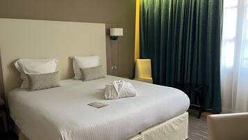 A hotel room with a large bed, two pillows, a bedside lamp, a chair, and a window with curtains.