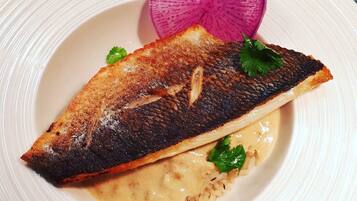 A plate with a grilled fish, a slice of radish, and a creamy sauce.