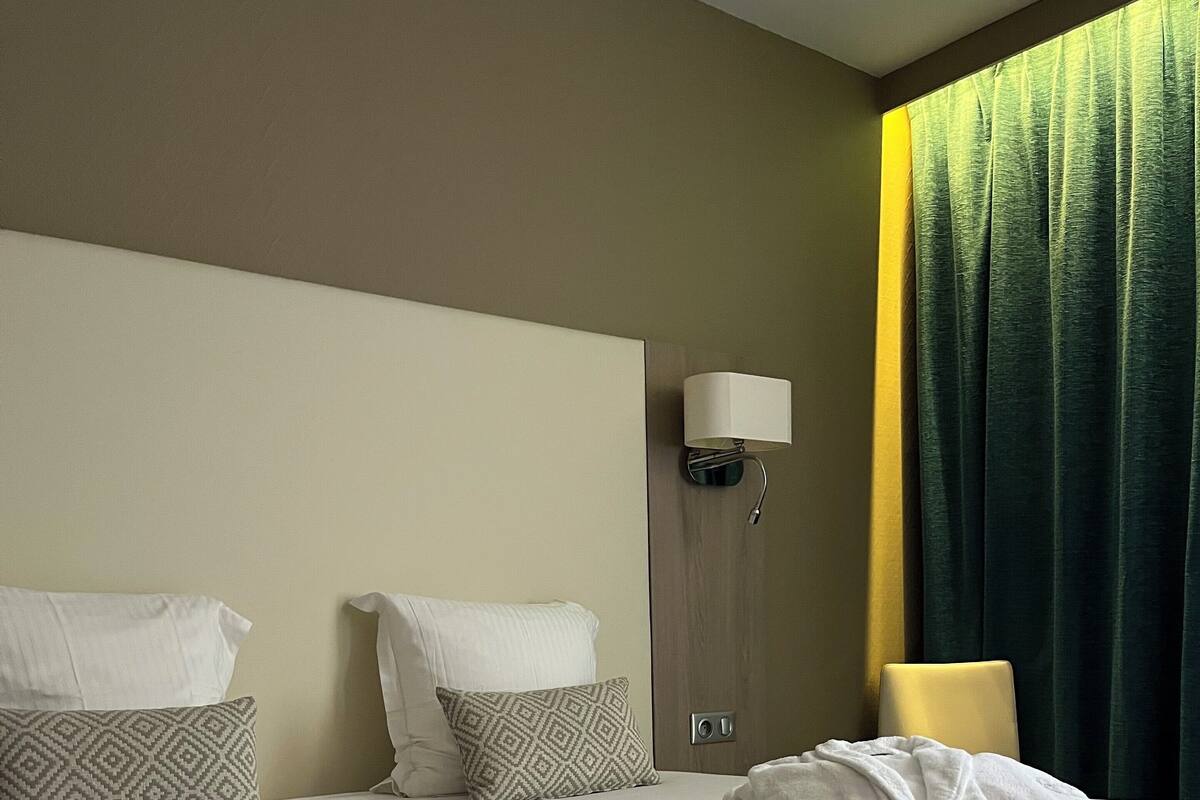 A neatly made bed with pillows, a bedside lamp, and a window with curtains.