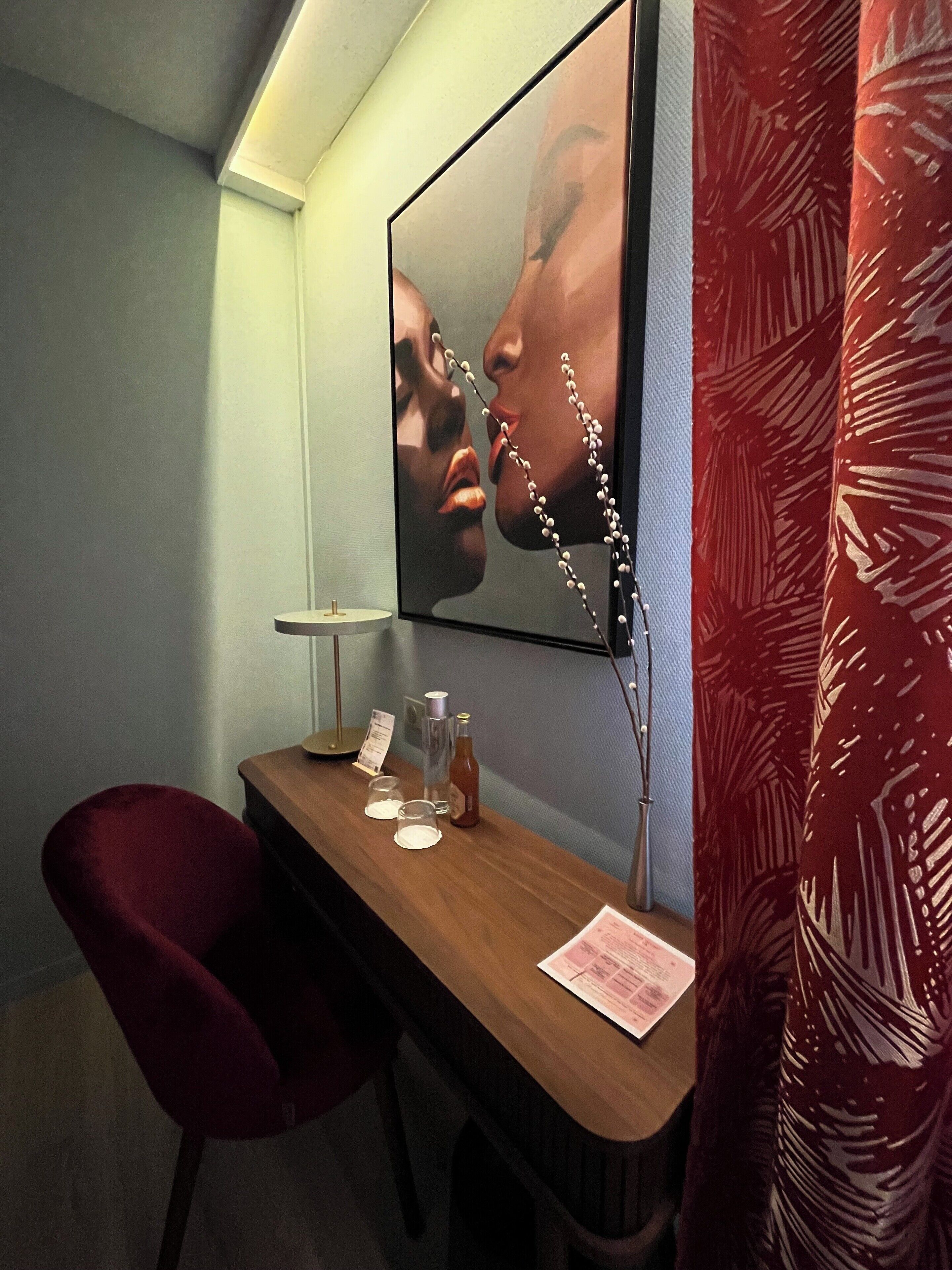 Una habitación de hotel con un escritorio de madera, un espejo, una silla roja y una cortina roja.