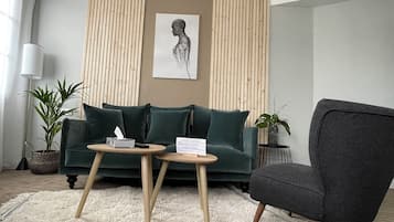 Una sala de estar moderna con un sofá verde, un sillón oscuro, una mesa redonda de madera y un tapete blanco.