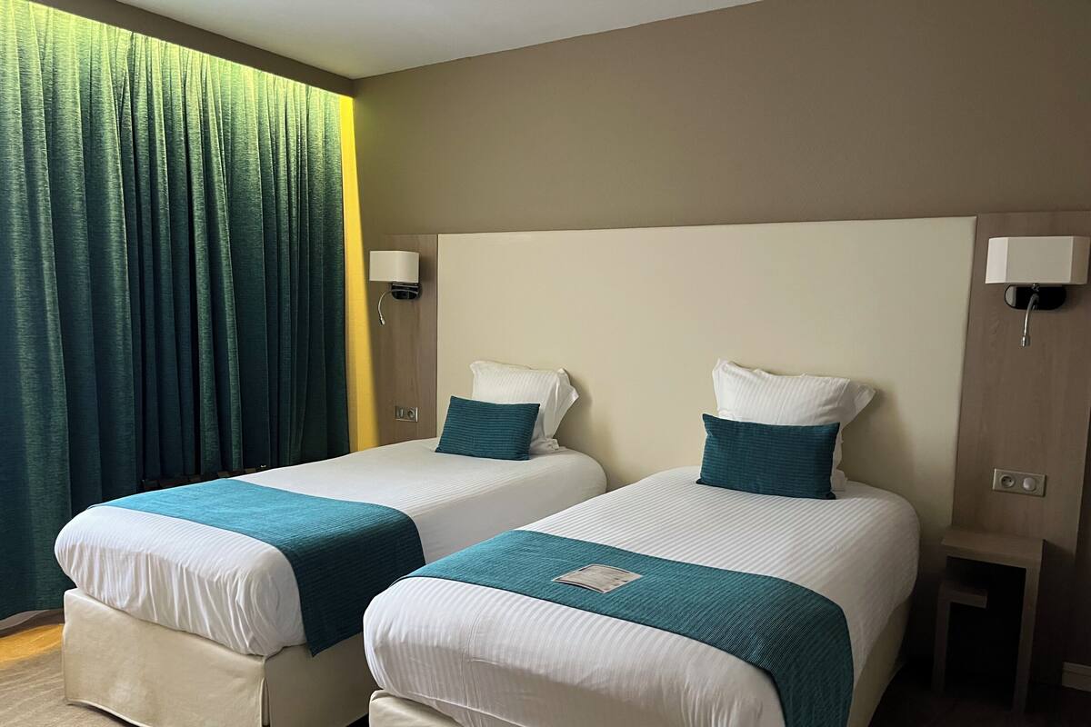 Two twin beds with white and teal bedding, a wooden headboard, and a small bedside table with a lamp.