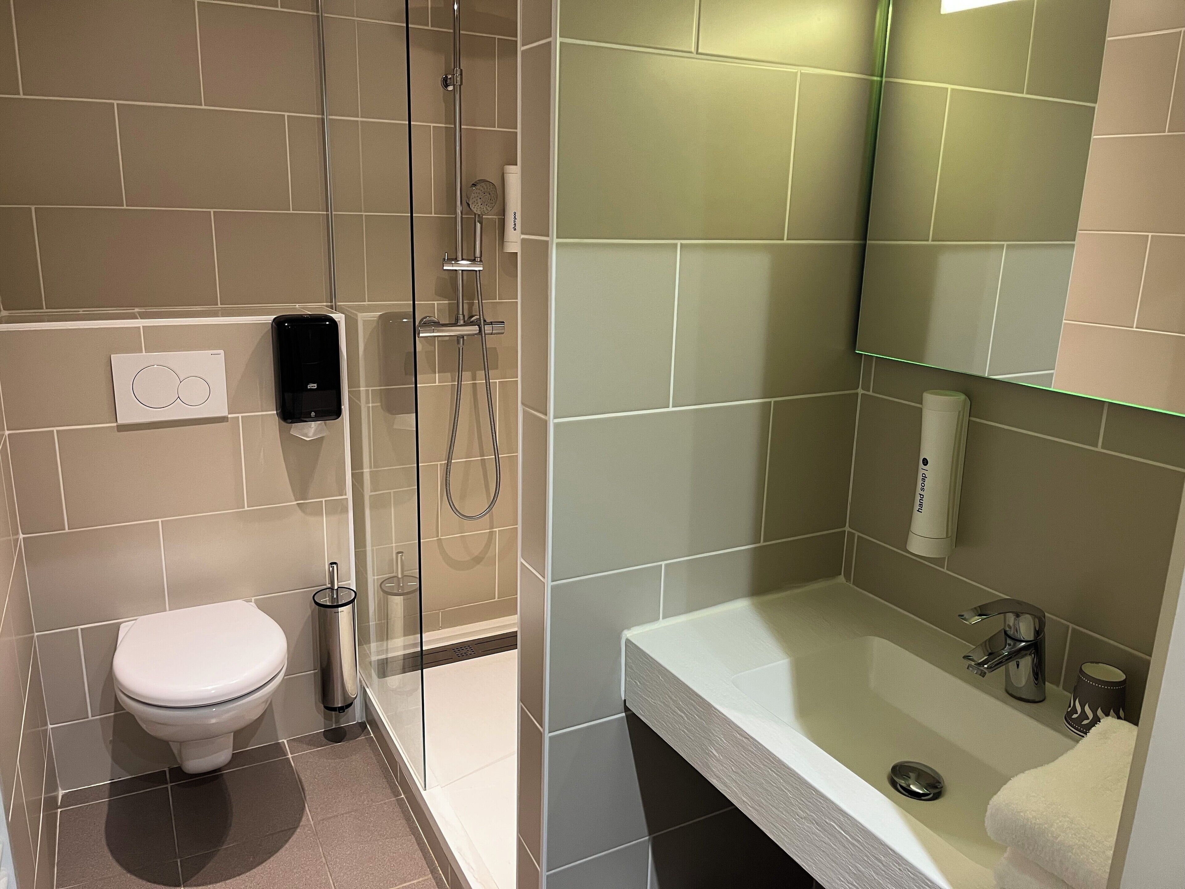 A modern bathroom with a toilet, a glass-enclosed shower, and a sink with a mirror.