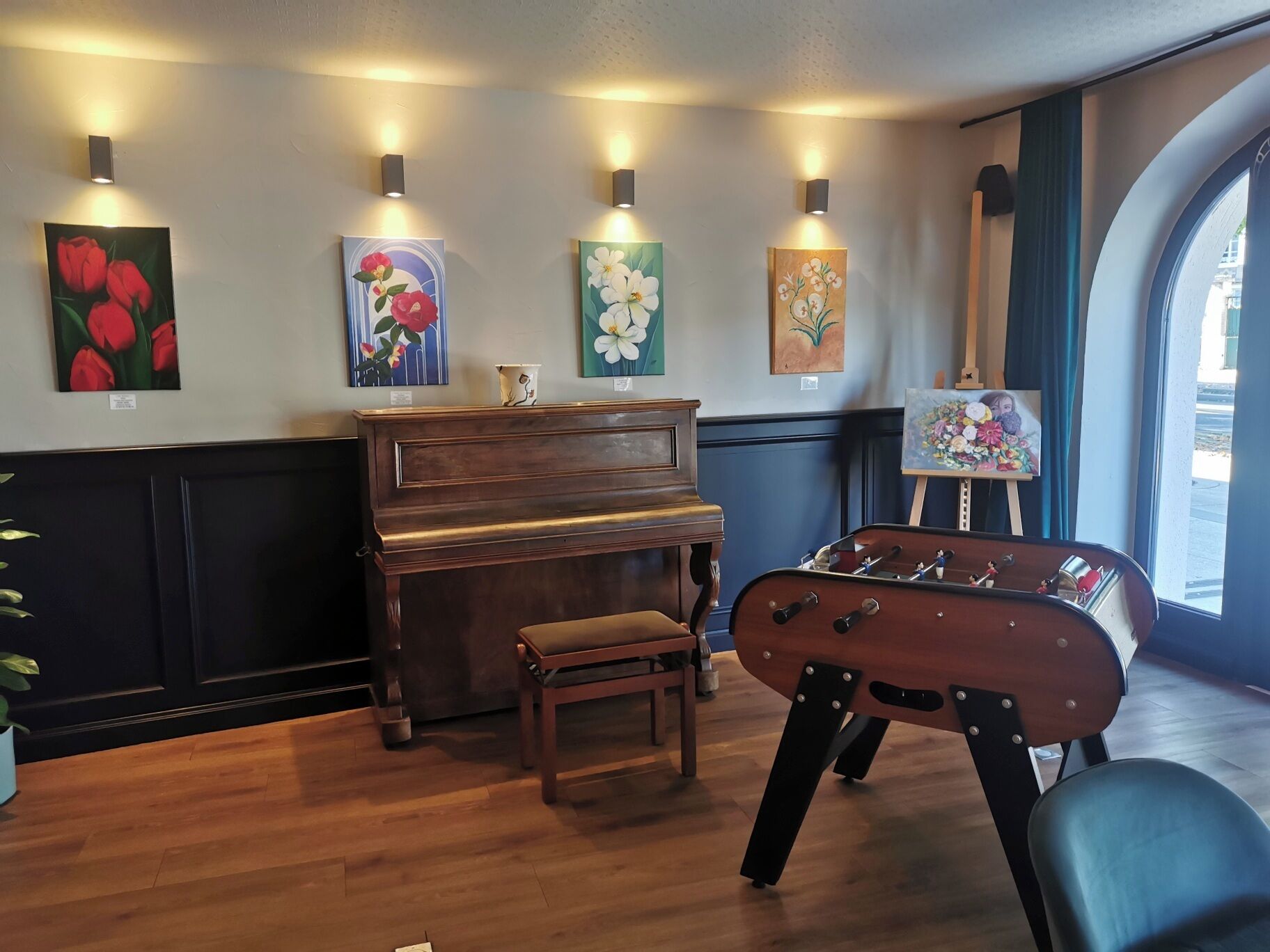 Une pièce avec un piano en bois, une table de baby-foot et des tableaux accrochés au mur.