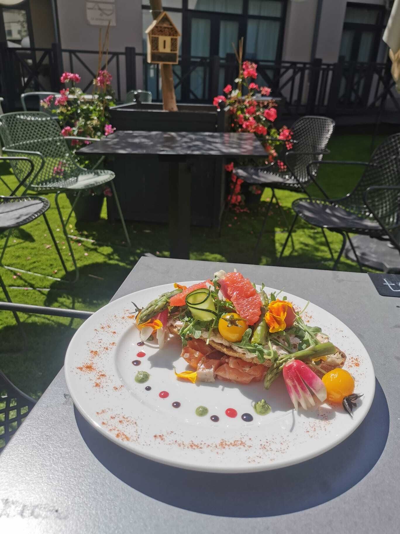 Une table à manger avec une assiette de nourriture, entourée de chaises et d’un petit espace jardin agrémenté de fleurs et d’une nichoir.