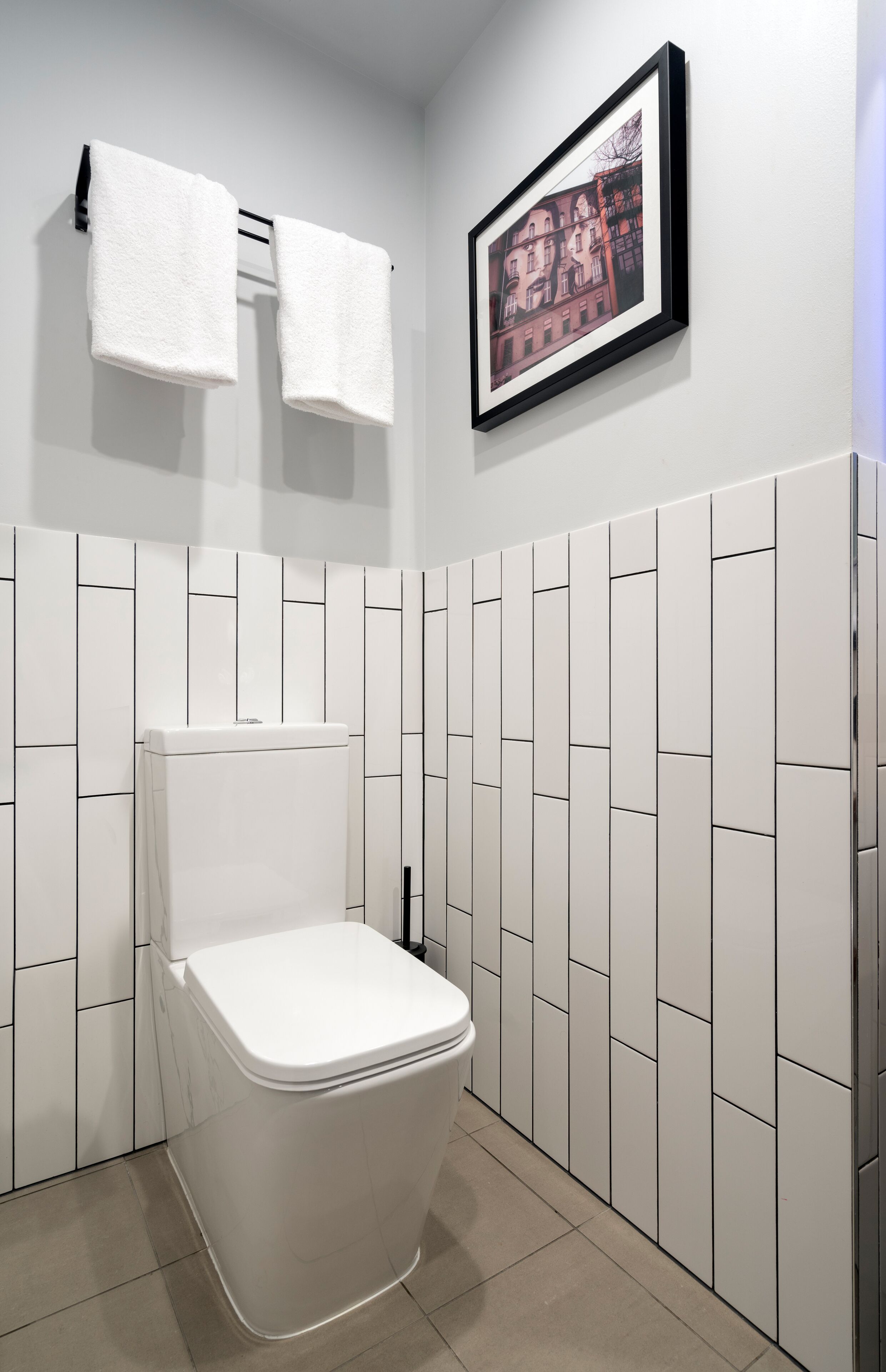 Ein modernes Badezimmer mit einer weißen Toilette, einem Handtuchhalter mit zwei weißen Handtüchern und einem gerahmten Bild an der Wand.