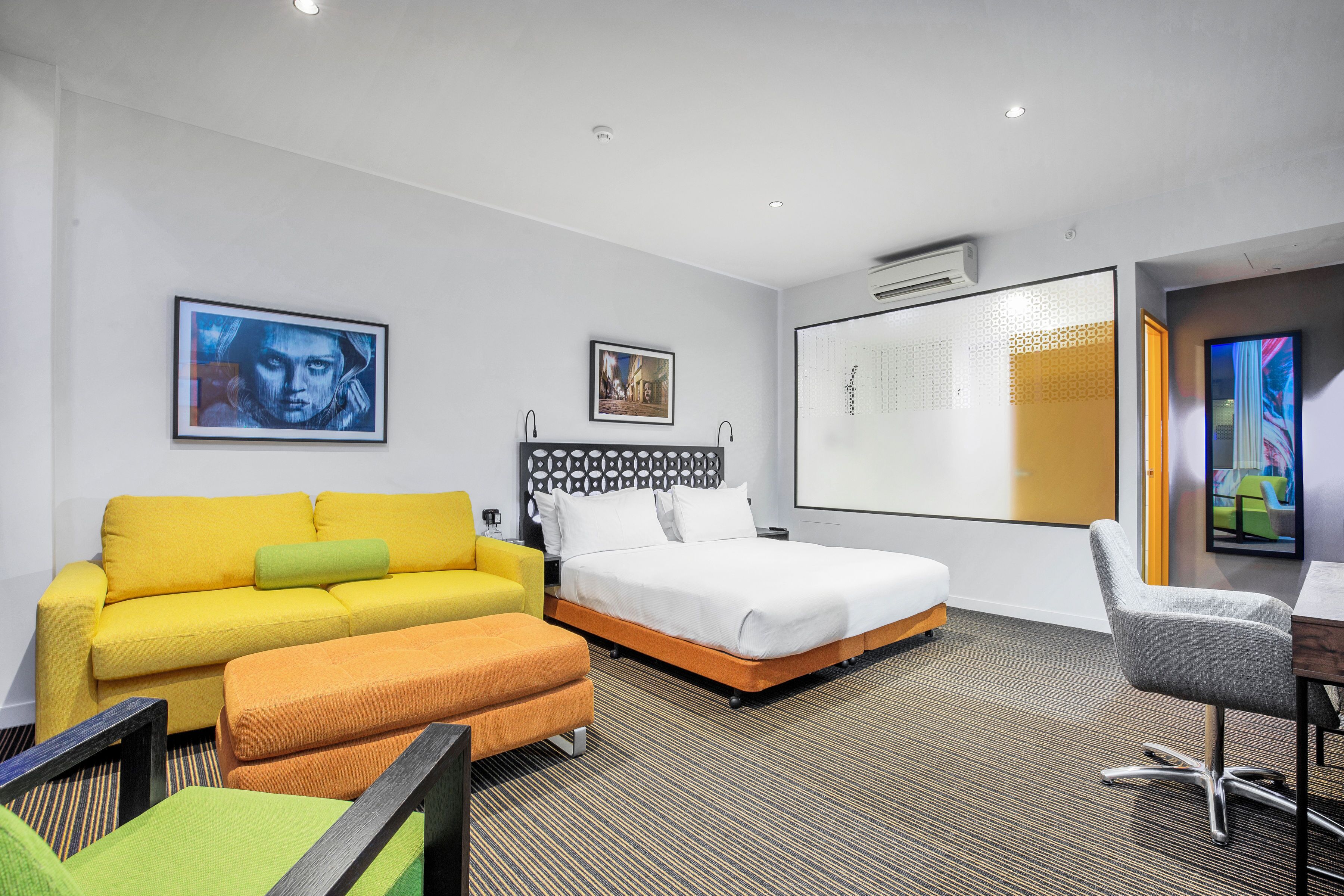 Une chambre d’hôtel comprenant un lit, un canapé, un pouf, un bureau et deux chaises.