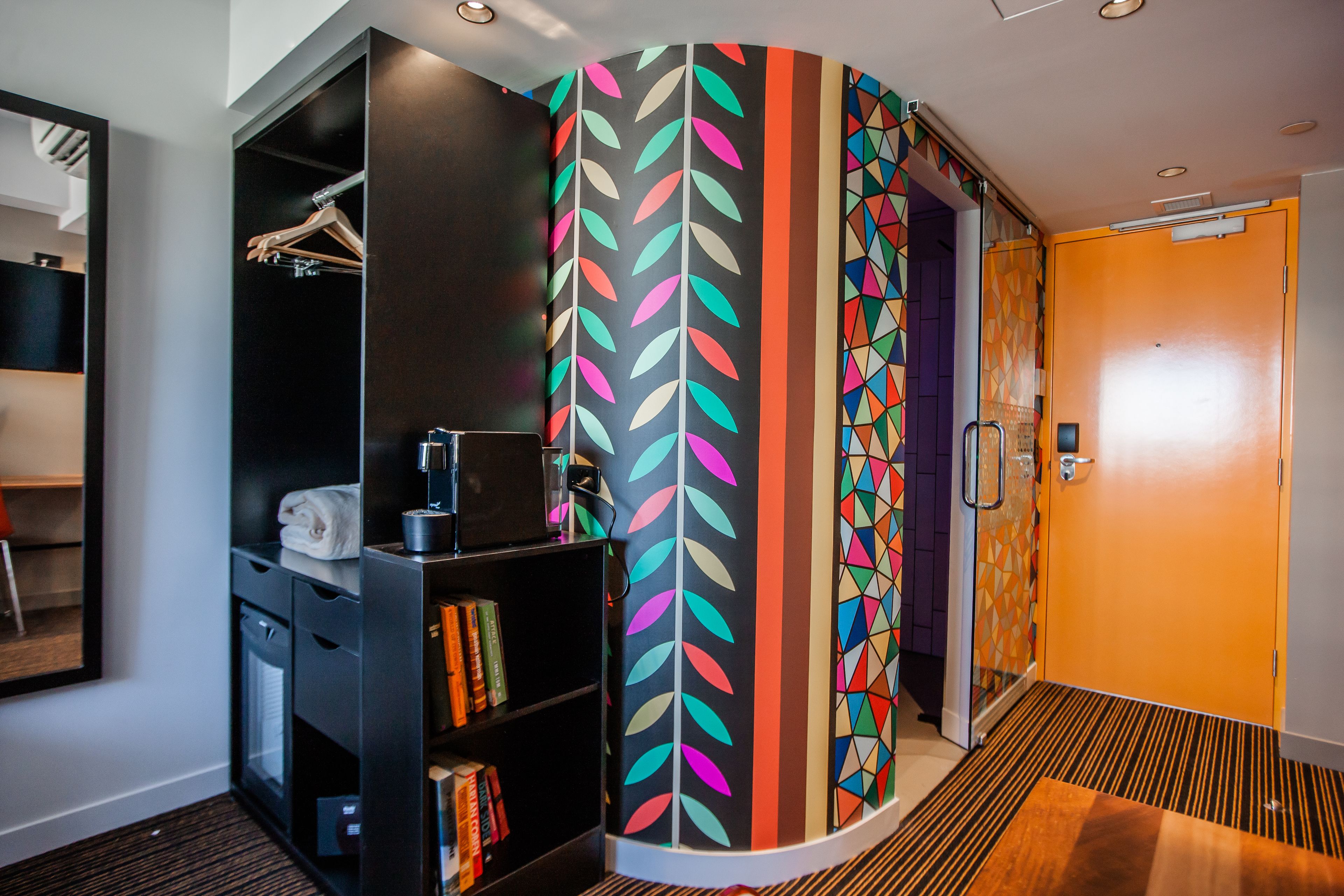 Una habitación de hotel moderna con una pared curva, una estantería, un perchero y una zona de ducha.