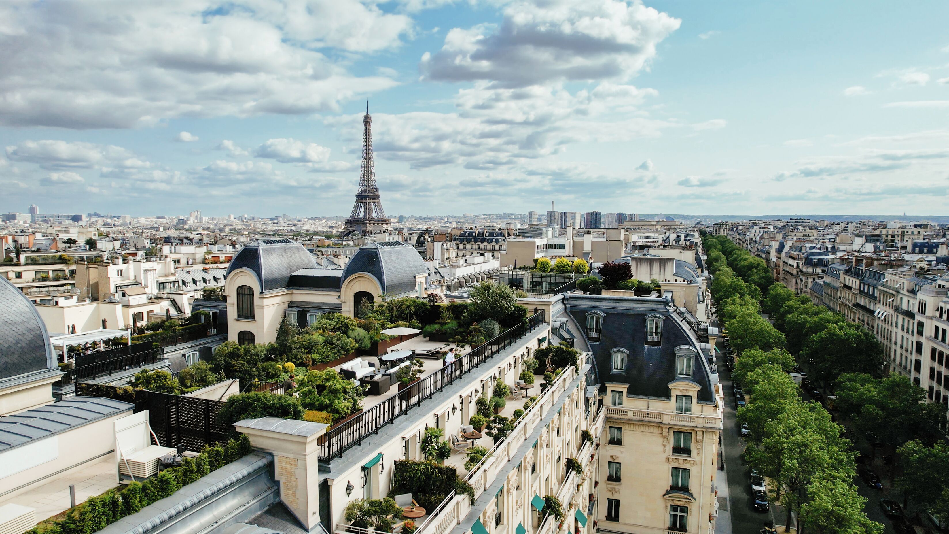 Un edificio de gran altura con jardín en la azotea, vista de la Torre Eiffel y un paisaje urbano de fondo.
