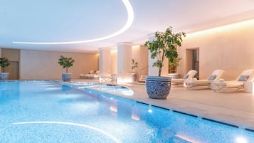 Ein moderner, überdachter Pool mit klarem, blauem Wasser, umgeben von Liegestühlen und Topfpflanzen.