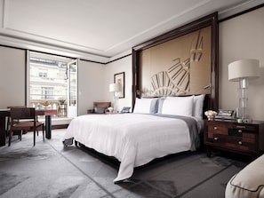 A hotel room with a large bed, a desk, a chair, a nightstand, and a view of the city through the window.