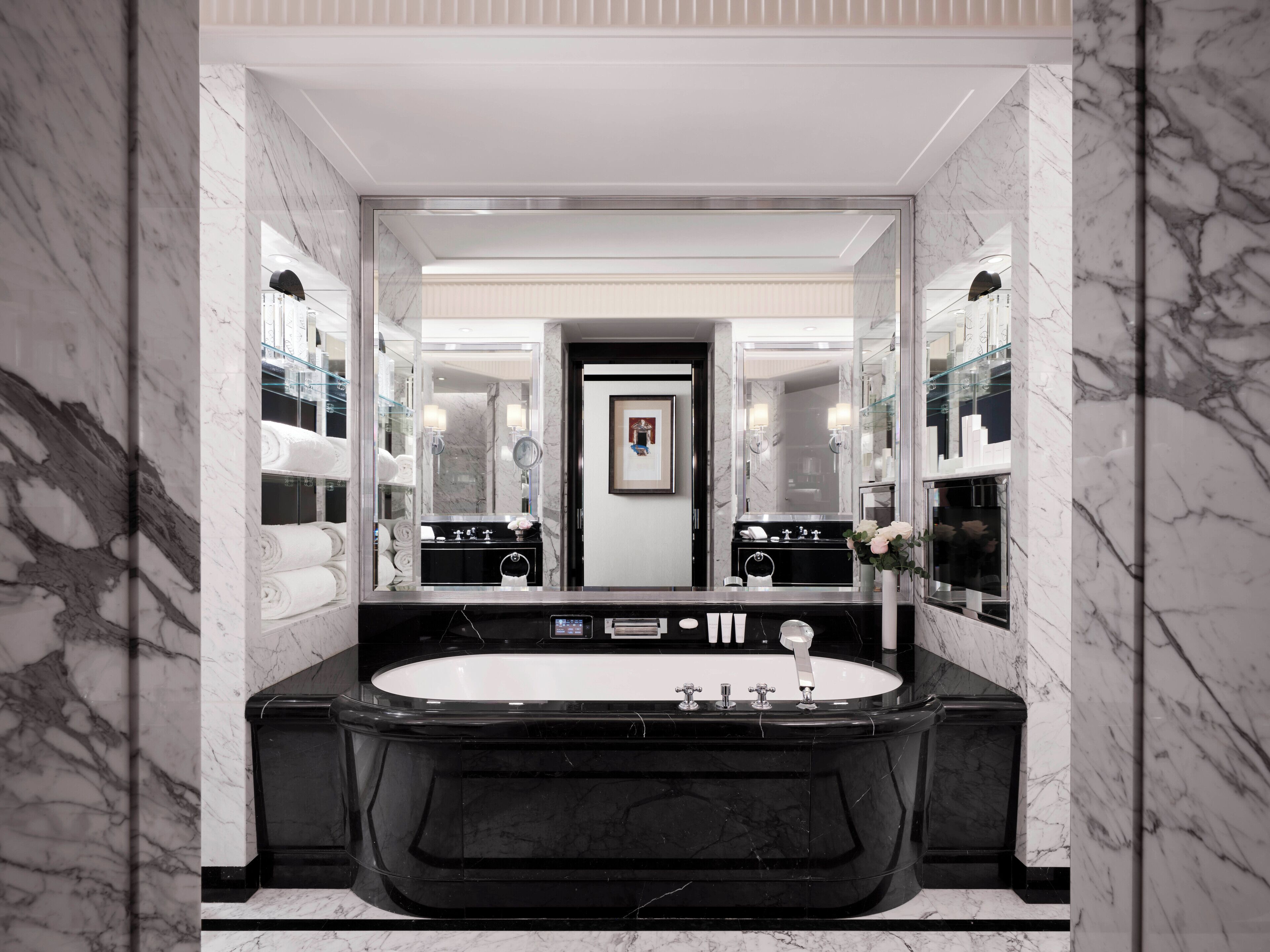 Un baño moderno con un espejo grande, lavamanos de mármol negro y una bañera blanca.