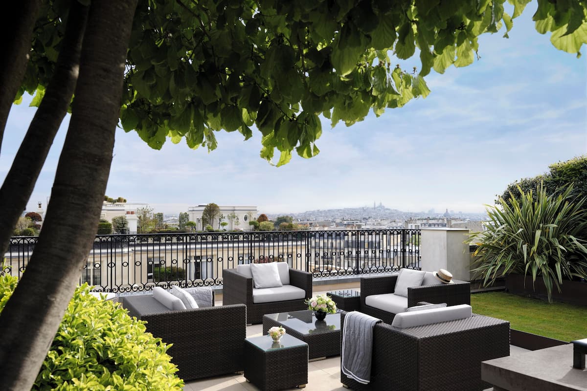 A rooftop terrace with wicker furniture, a view of the cityscape, and a clear sky.