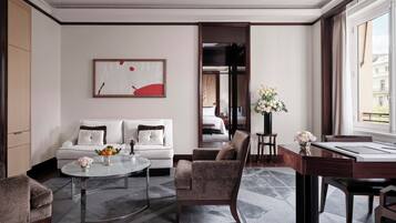 Une chambre d’hôtel moderne, dotée d’un canapé, d’un fauteuil, d’une table à manger et offrant une vue sur la ville grâce à de grandes fenêtres.