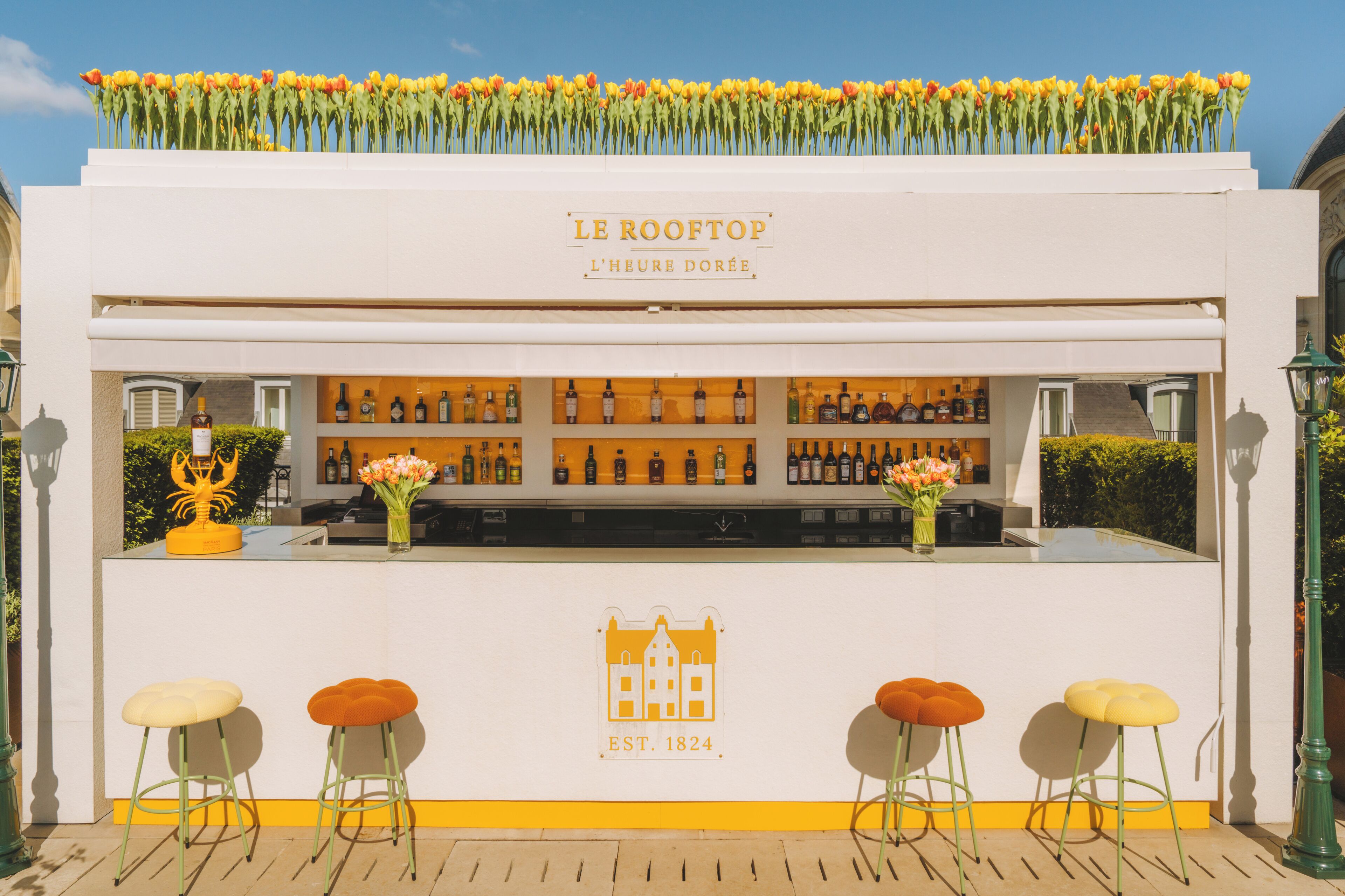 A bar named 'Le Rooftop' with a white exterior, a flower arrangement on top, and a sign indicating it was established in 1824.