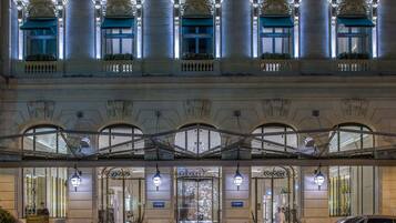 La façade d’un hôtel présente une architecture classique, de grandes fenêtres en arc de cercle et une entrée abritée.