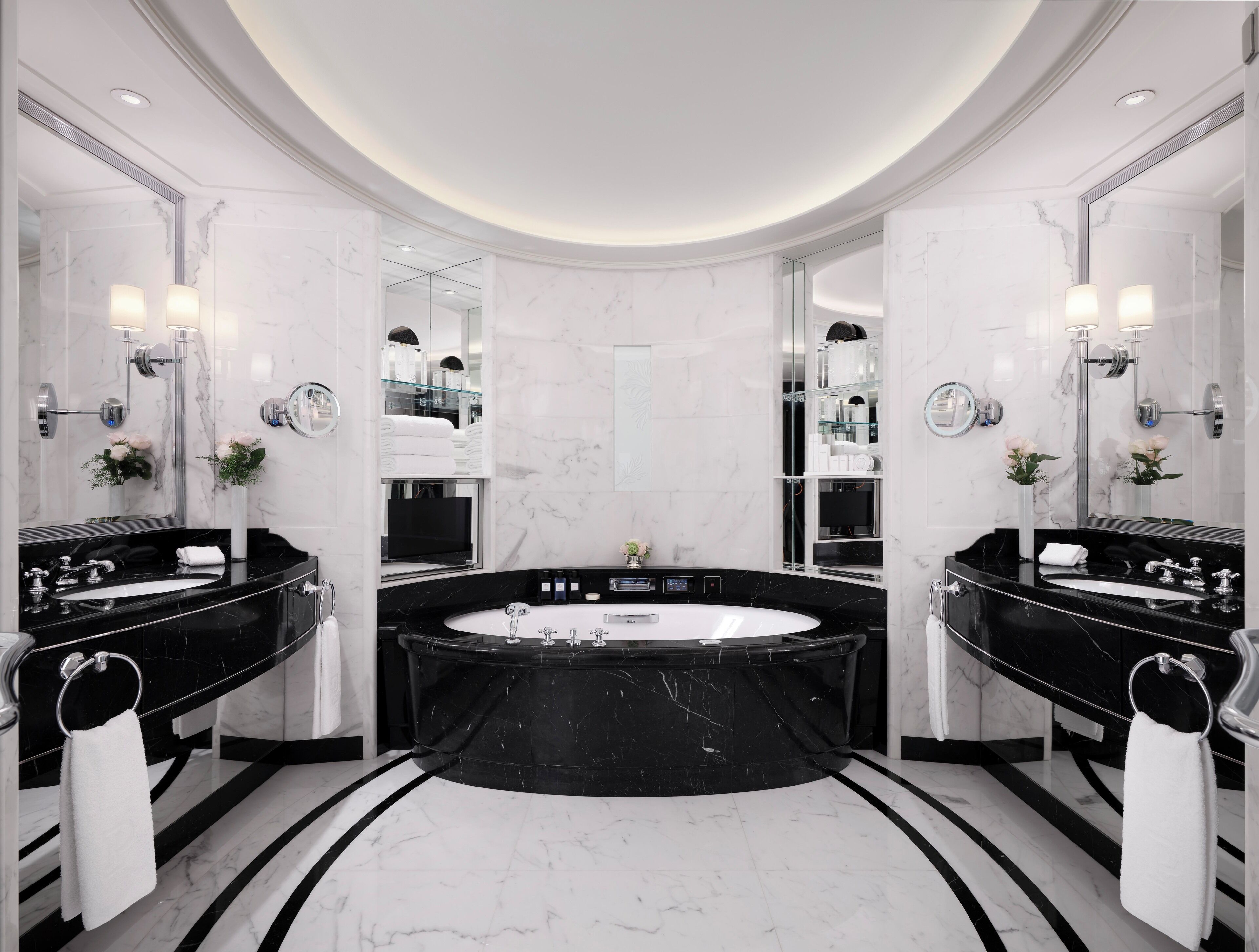 Ein luxuriöses Badezimmer mit einer großen, zentral platzierten Badewanne, zwei separaten Waschbecken und einem großen Spiegel.