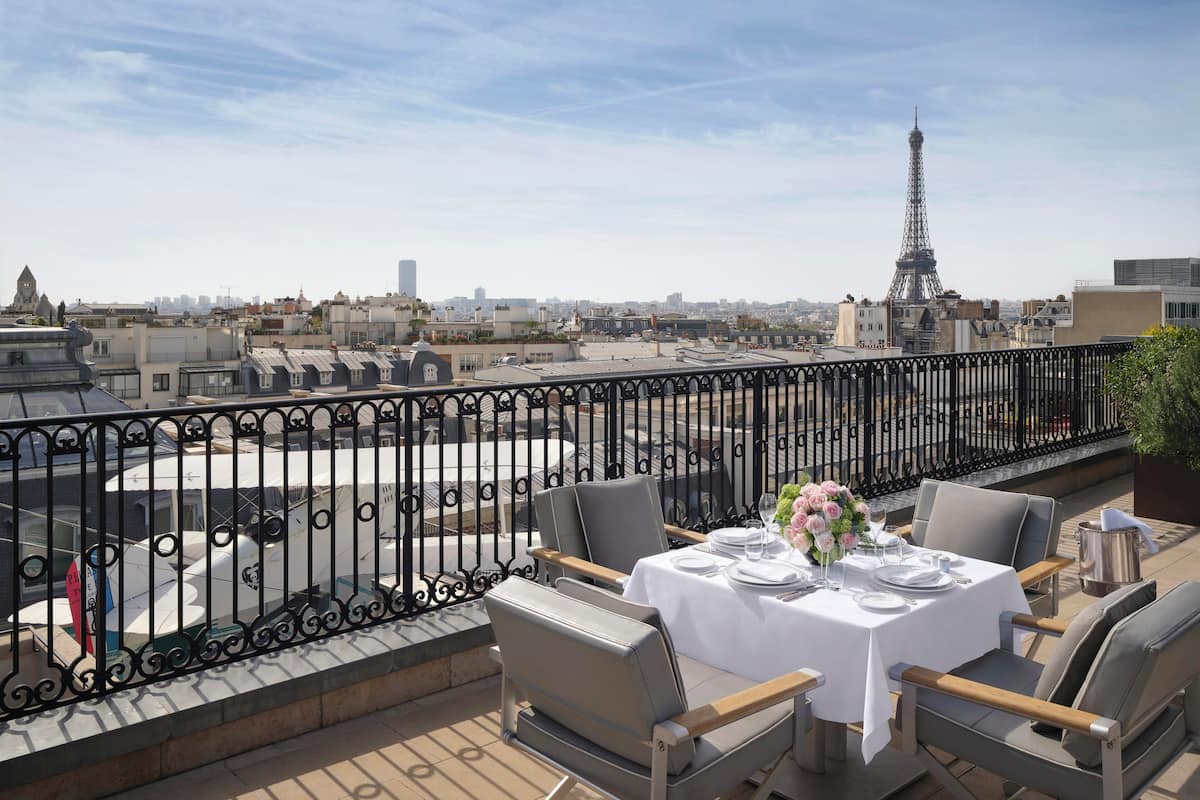 A rooftop terrace with a table set for dining, overlooking a cityscape with the Eiffel Tower in the distance.