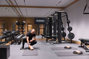 A gym with weightlifting equipment, exercise mats, and a sign reading "The Peninsula SPA & WELLNESS CENTRE".