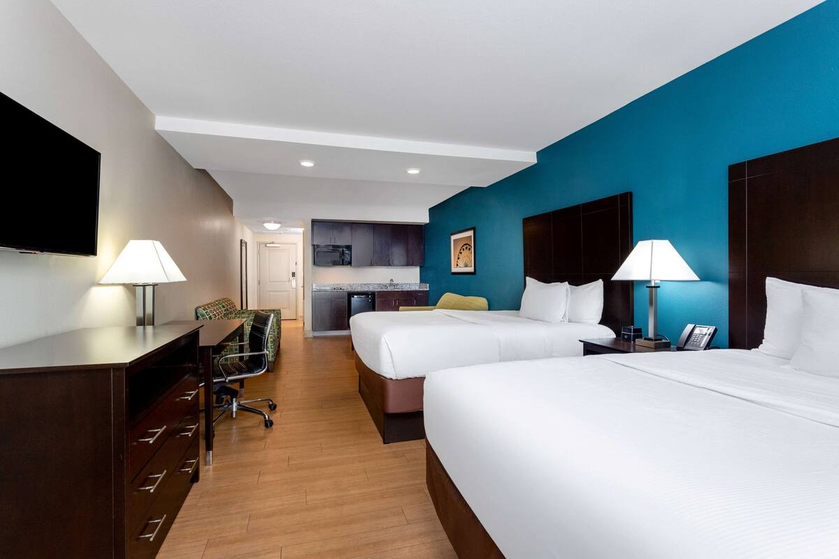 Une chambre d’hôtel avec deux lits, un bureau, une chaise, une télévision et, au fond, une petite cuisine.
