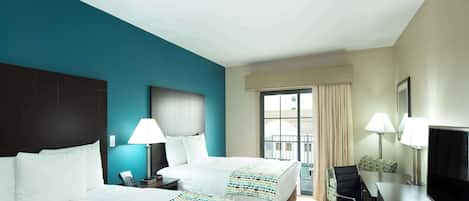 A hotel room with two beds, a desk with a TV, and a chair.