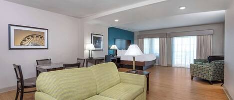 A hotel room with a green sofa, a dining table with chairs, a TV, and a bed with curtains.