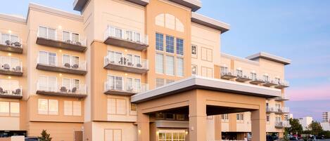 A multi-story hotel with a beige facade, balconies, and a covered entrance.