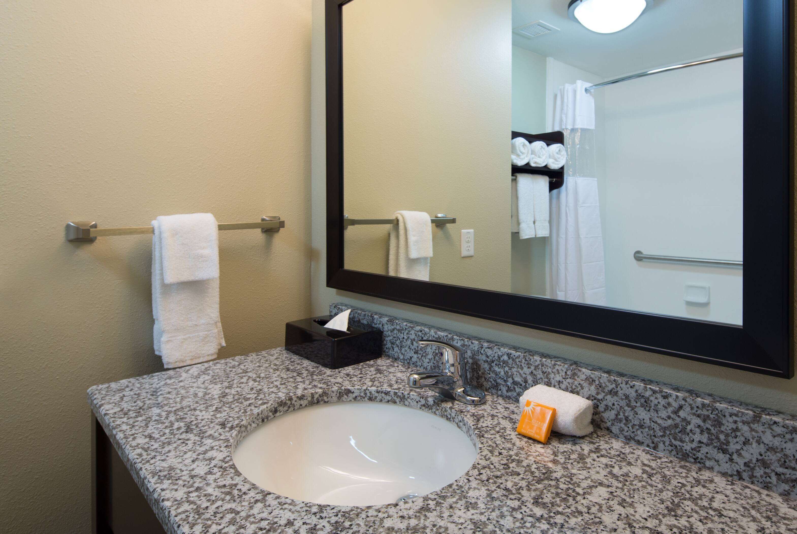 A bathroom with a granite countertop, a white sink, a mirror, and a towel rack with folded towels.