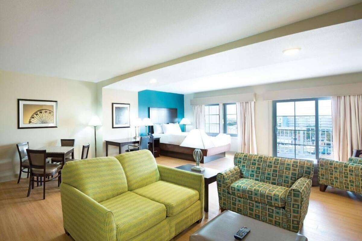 Une chambre d’hôtel avec un canapé vert, un fauteuil à motifs, un lit, un bureau et une table à manger.
