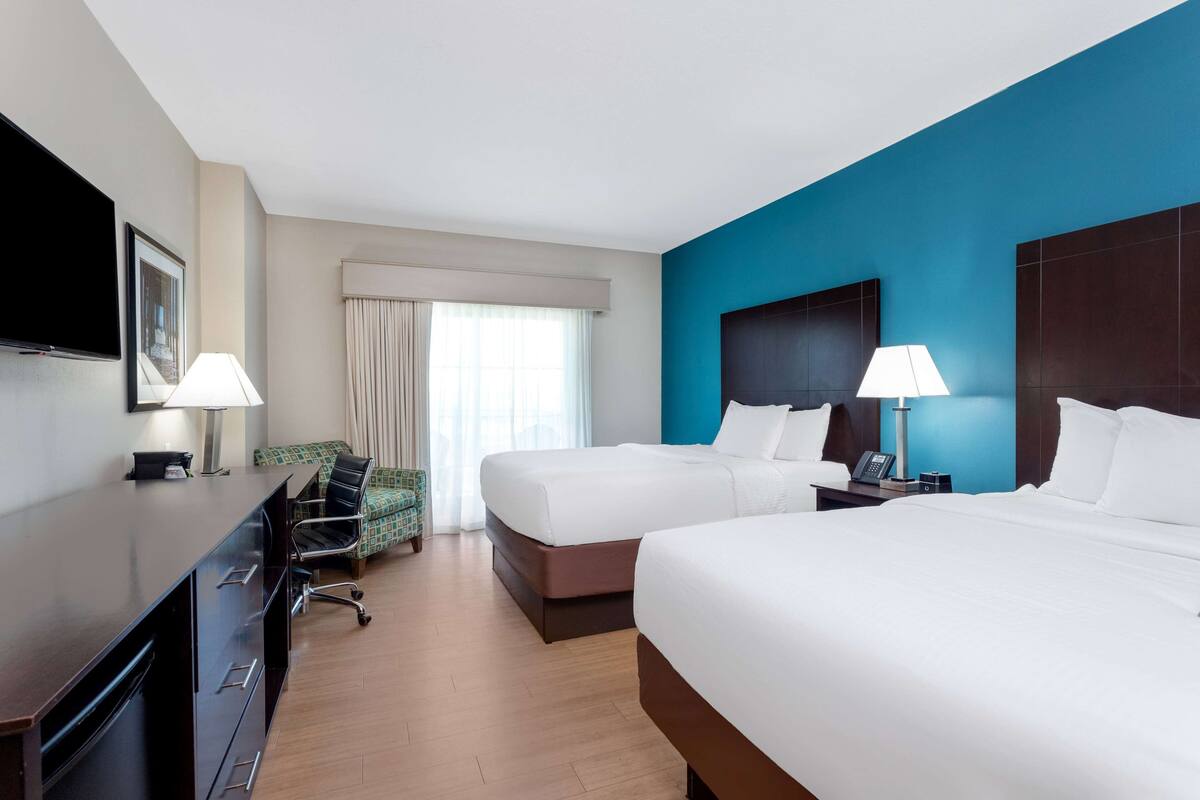 Une chambre d’hôtel avec deux lits, un bureau, une chaise, une télévision et une fenêtre avec des rideaux.