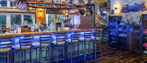 A bar with multiple stools, shelves with bottles, and a staircase.