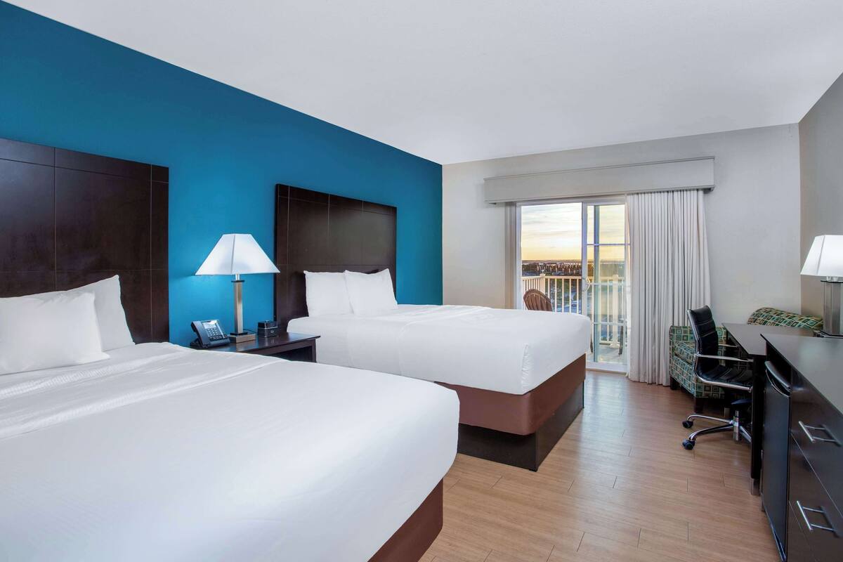 Une chambre d’hôtel avec deux lits, un bureau, une chaise, un téléphone et une vue sur la ville par la fenêtre.