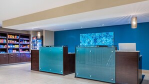 Een receptiegedeelte met een blauwe wand, een groot televisiescherm en een bar met diverse snacks.