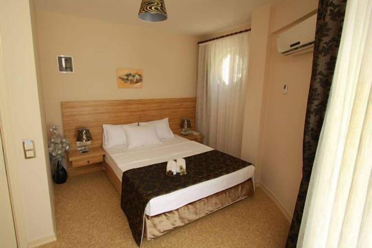 Une chambre d’hôtel avec un lit, une table de chevet, une lampe, un tableau au mur et une fenêtre avec des rideaux.