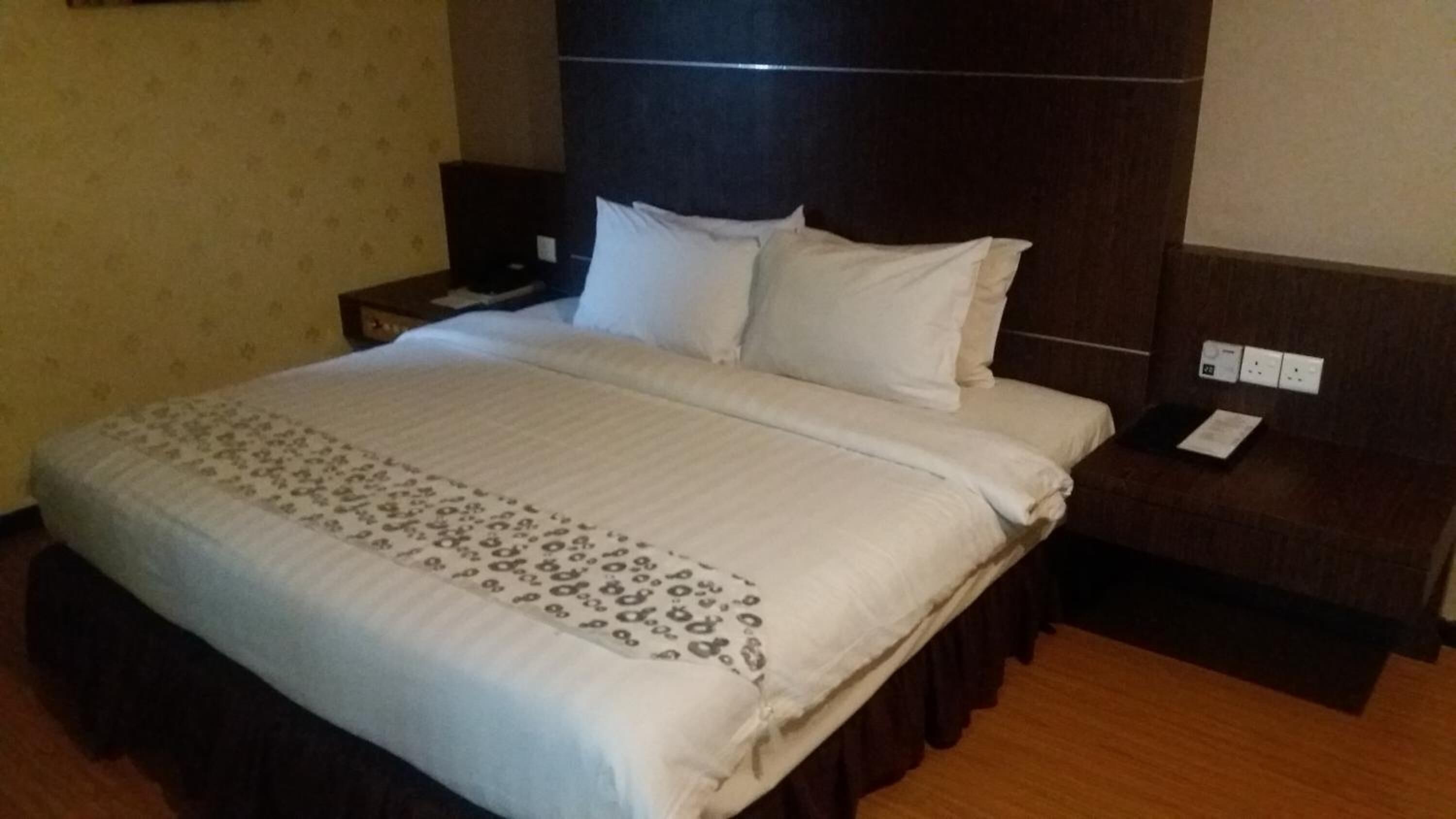 A hotel room with a large bed, a nightstand, a bedside table, and a wall socket.