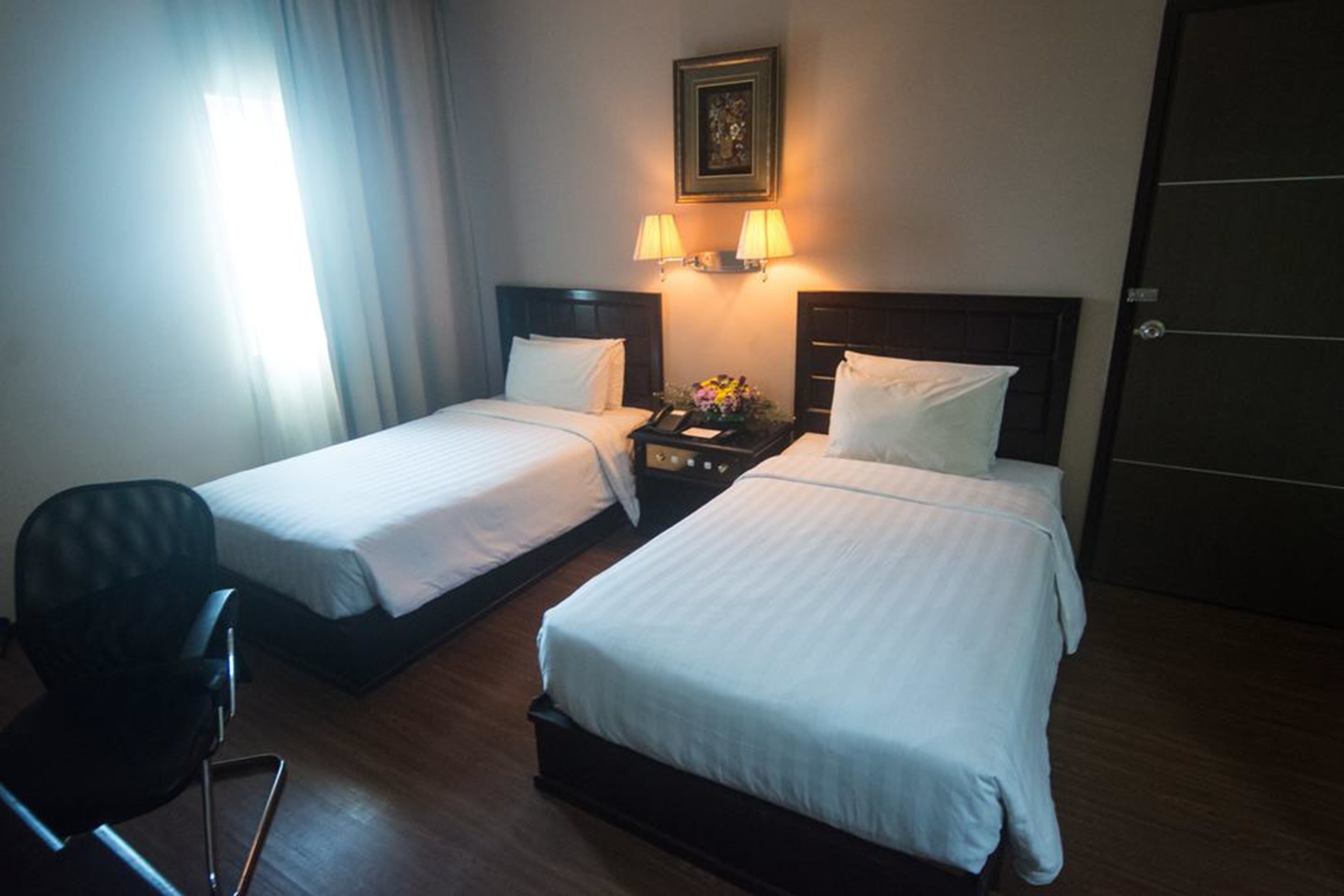 Una habitación de hotel con dos camas individuales, una mesita de noche con lámparas, una silla y una puerta.