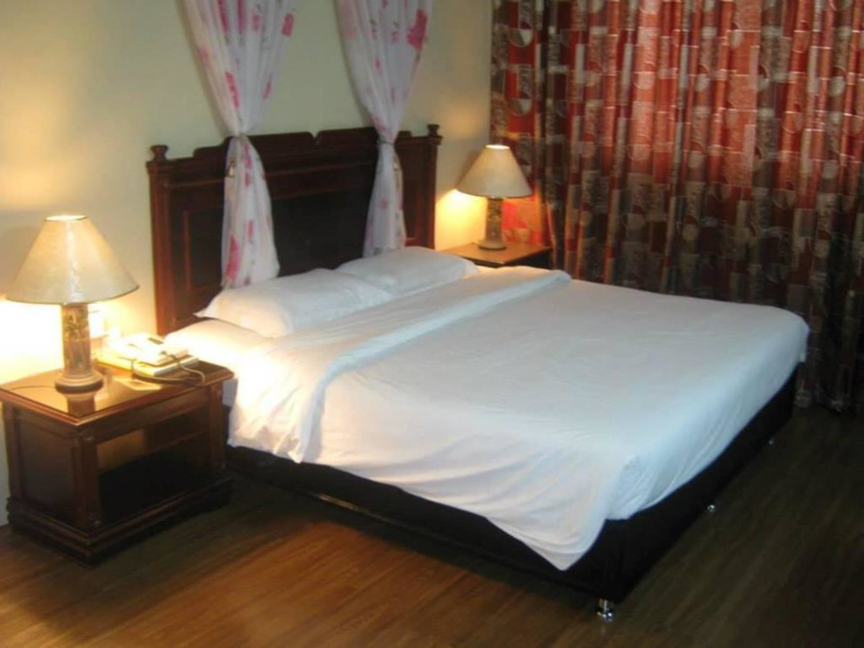 A neatly made bed with white linens, two bedside lamps, and a wooden nightstand.
