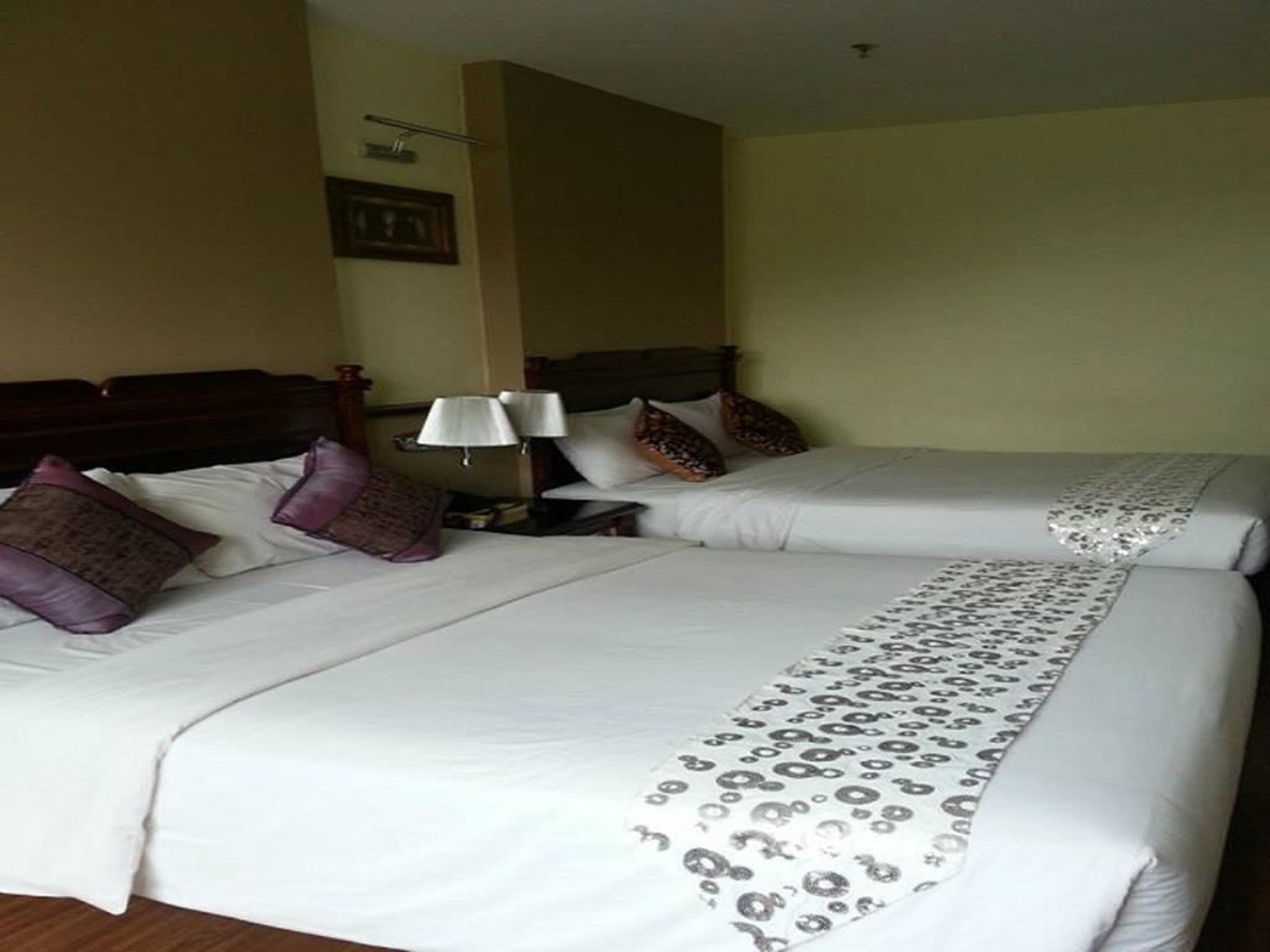 A hotel room with two beds, each with white linens and decorative pillows. There is a nightstand with a lamp between the beds.