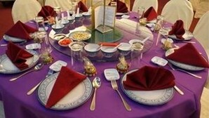 A round dining table set with white chairs, red napkins, and a purple tablecloth.
