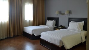 A hotel room with two beds, wooden flooring, and a window with curtains.