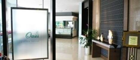 Zona de recepción de un hotel con puerta de cristal, mostrador de recepción y un panel en la pared.