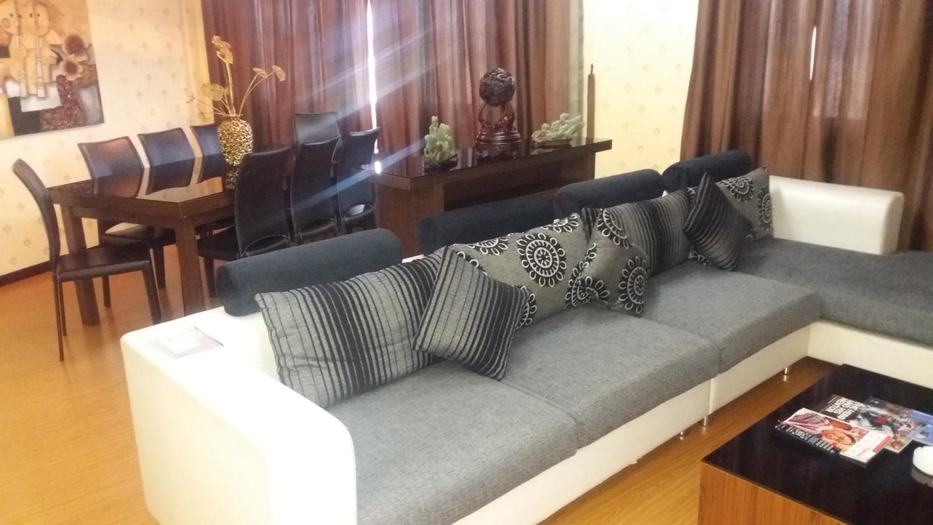 A modern living room with a grey sectional sofa, black and white patterned cushions, a white coffee table, and a wooden dining table with chairs.