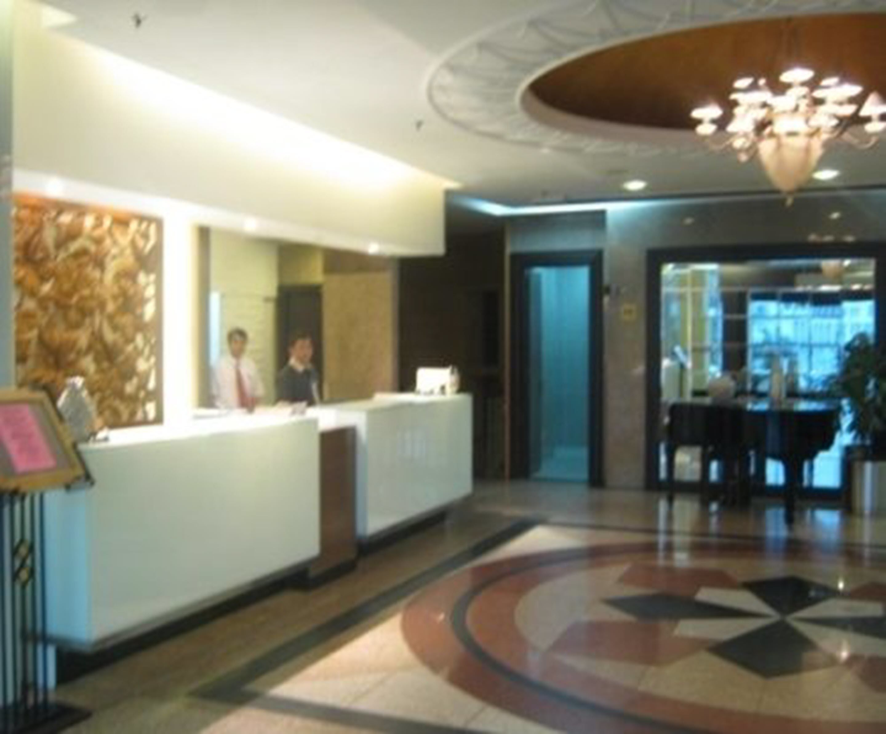 A hotel reception area with a modern design, including a reception desk, a chandelier, and a patterned floor.