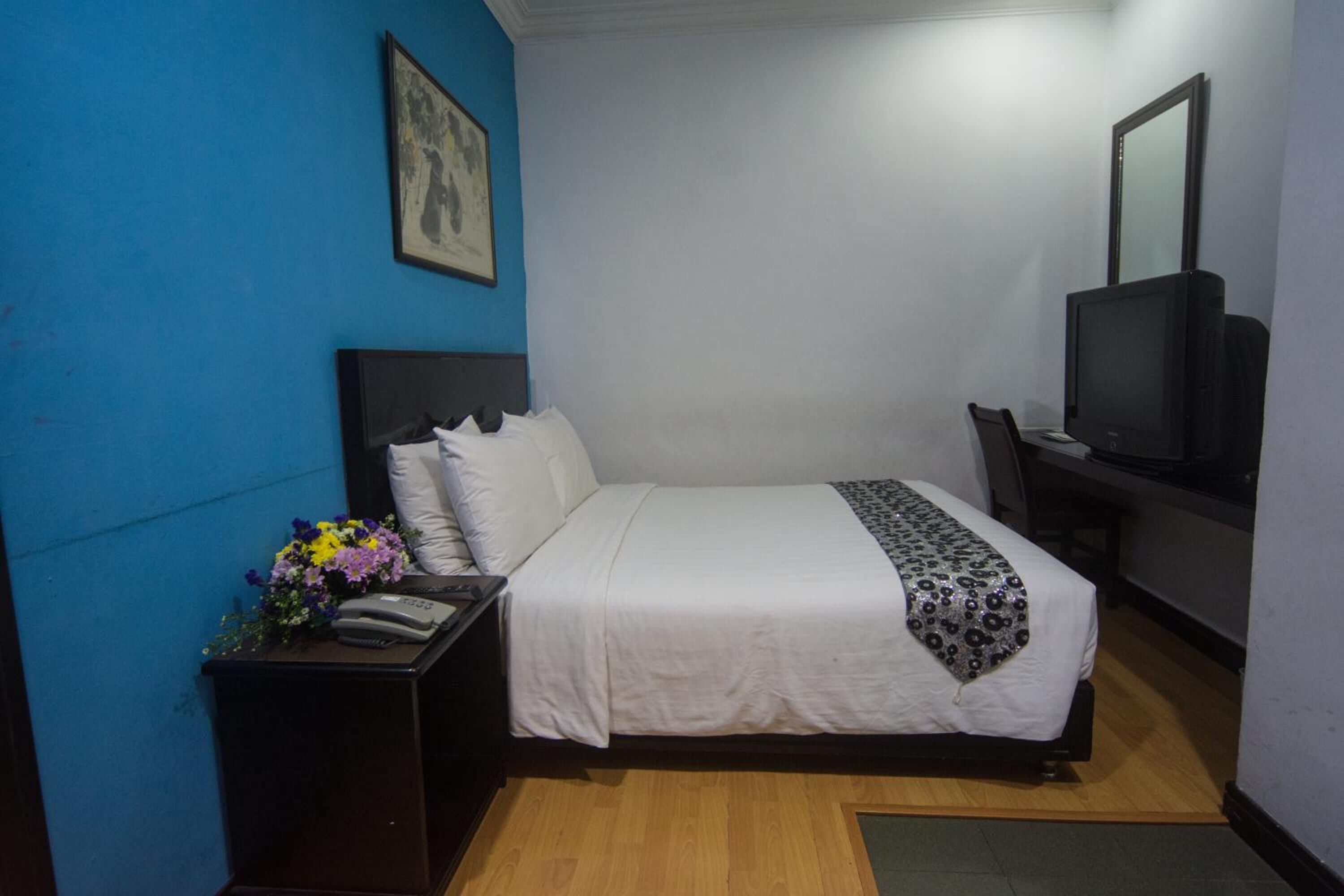 A hotel room with a bed, a desk with a computer, a television, and a wall-mounted mirror.