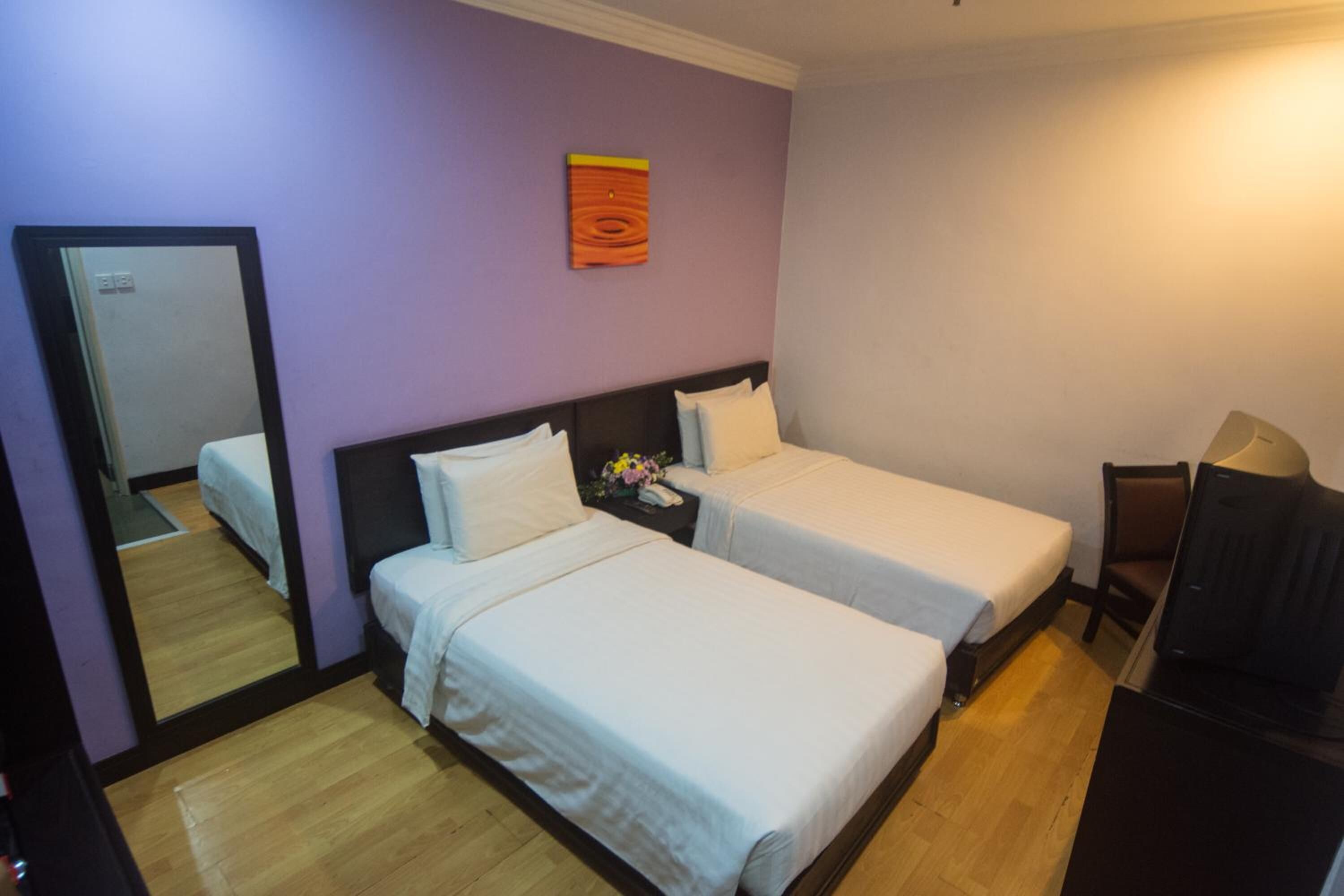 Una habitación con dos camas individuales, un escritorio, una silla, un espejo y una mesita de noche con un florero.
